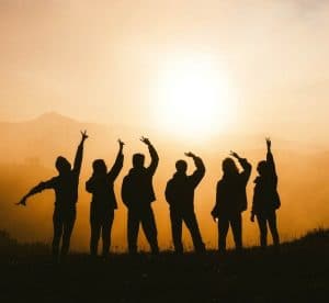 group of people standing on a mountain waving at a sunrise, showcasing community 